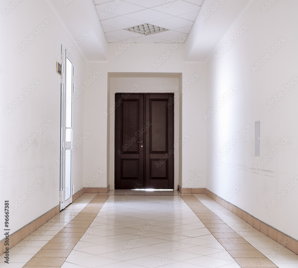 White hallway with marble floor and brown door in hospital background