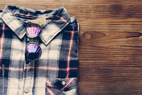 Men's plaid shirt and colored glasses on a wooden background