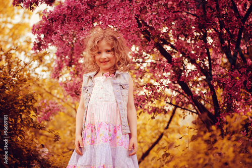 happy child girl in pink dress playing outdoor in spring garden near blooming crabapple tree