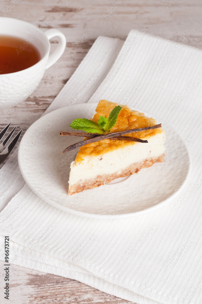 Vanilla cheesecake on a white plate and cup of tea, vertical