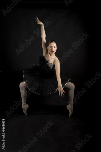Fototapeta Naklejka Na Ścianę i Meble -  Beautiful expressive ballerina in the role of a black swan, wearing black tutu and pointe shoes on black background