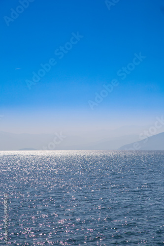 Seascape with blue sky and waters, with distant land hidden in the mist.