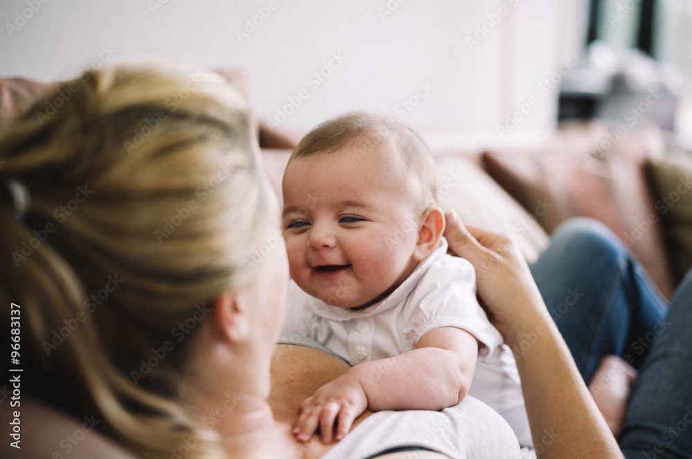 A woman lying on a sofa playing with a baby girl. A woman lying on a sofa playing with a baby girl.