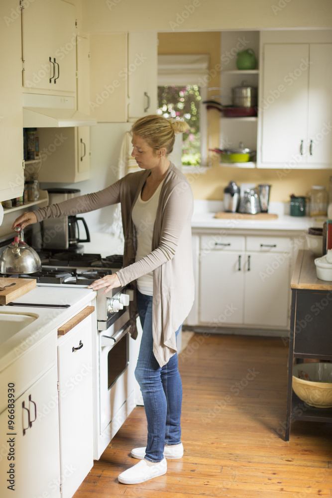 Woman standing in a kitchen, placing a kettle on a stove. Woman standing in a kitchen, placing a kettle on a stove.