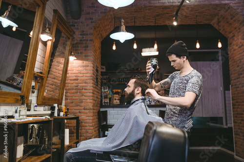 Young hairdresser drying man's hair with blowdryer