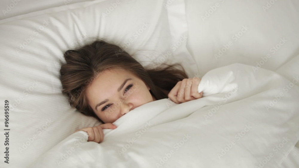Young woman lying in bed pulling up blanket and smiling at camera. Panning camera Young woman lying in bed pulling up blanket and smiling at camera. Panning camera