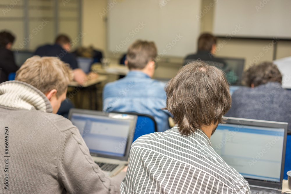 Informatics workshop at university. Rear view of students sitting and listening in lecture hall doing practical tasks on their laptops. Informatics workshop at university. Rear view of students sitting and listening in lecture hall doing practical tasks on their laptops.