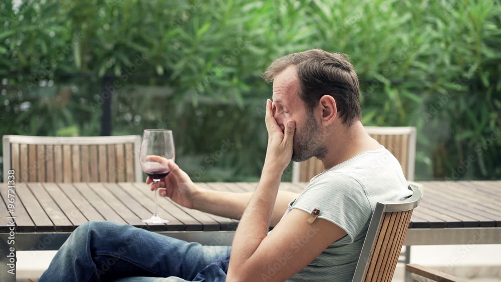 Sad, depressed man drinking wine on terrace
