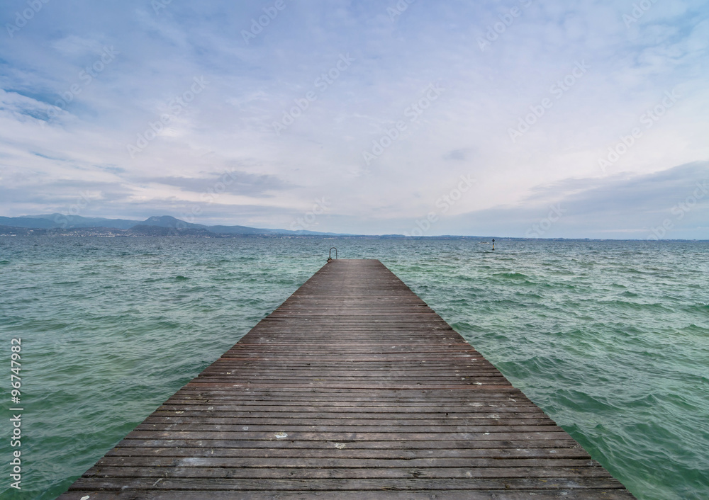 wooden pier and cloudy sky over Garda lake - Italy