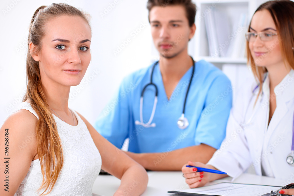 Happy blond female patient next to a few doctors in hospital sitting at the table