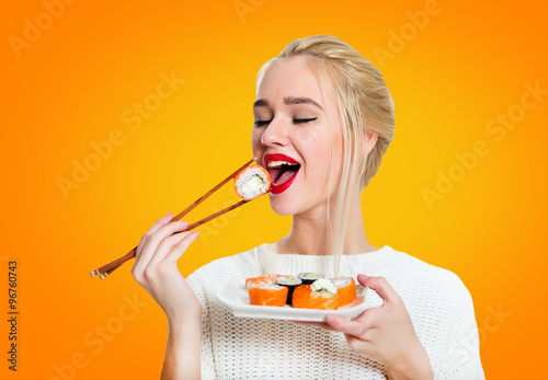 Young woman holding sushi with a chopsticks, isolated on yellow