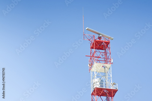 Radar antenna on a metal structure colored in red and white against a blue background