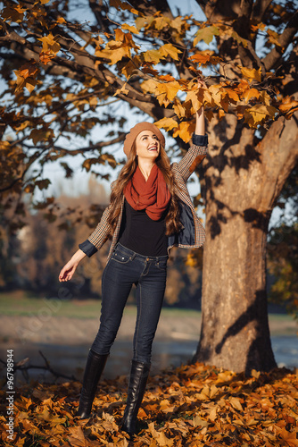 slender young brunette beautiful girl with long hair in a beret with a scarf and coat walks in autumn park with a lot of yellow and orange leaves