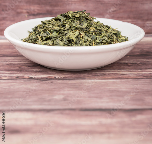 Dried Japanese green tea leaves in white bowl over wooden background