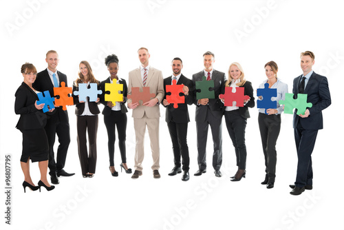 Portrait Of Happy Business Team Holding Jigsaw Pieces