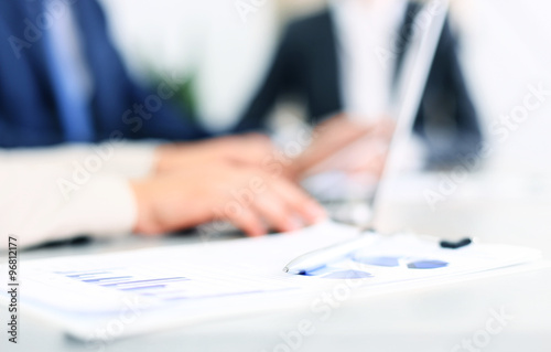 Documents with chart and graph and pen on background of two employees working