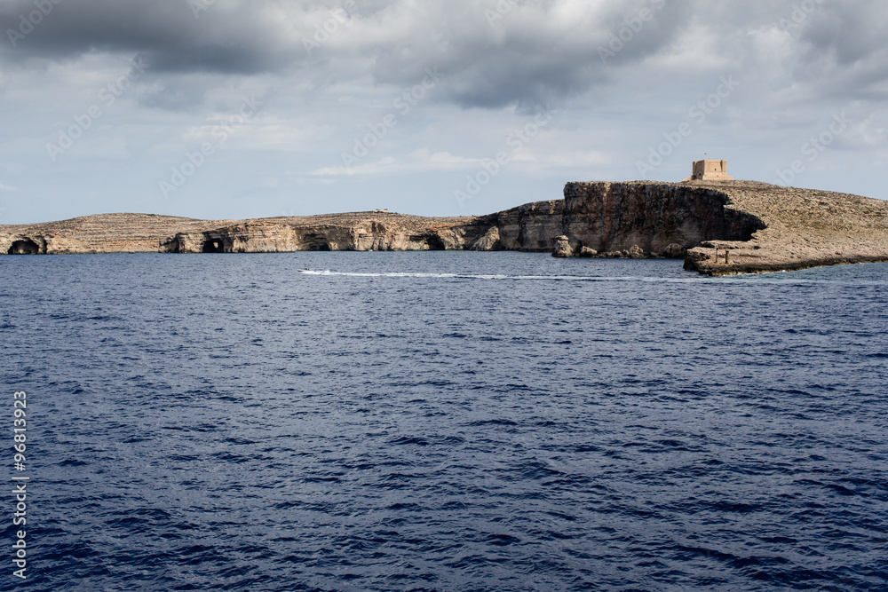 Comino island with St. Mary's Tower and dark storm clouds