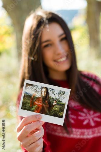 Young woman holding an instant photo print where she is happy