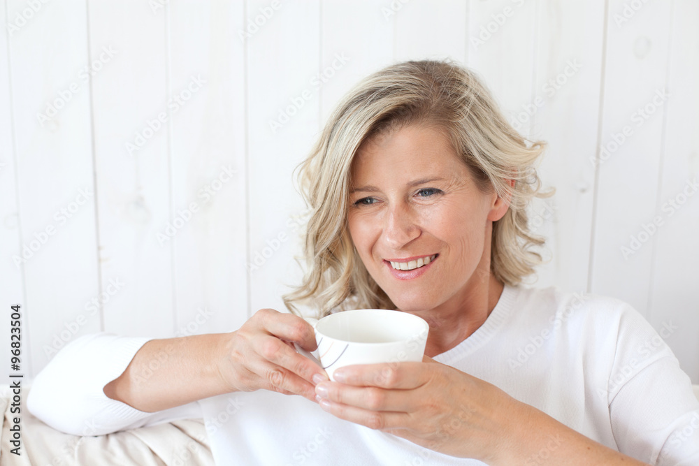 beautiful adult woman with blond hair, smiling, happy drinking coffee, tea.He is sitting on the sofa with a cup in hand. 