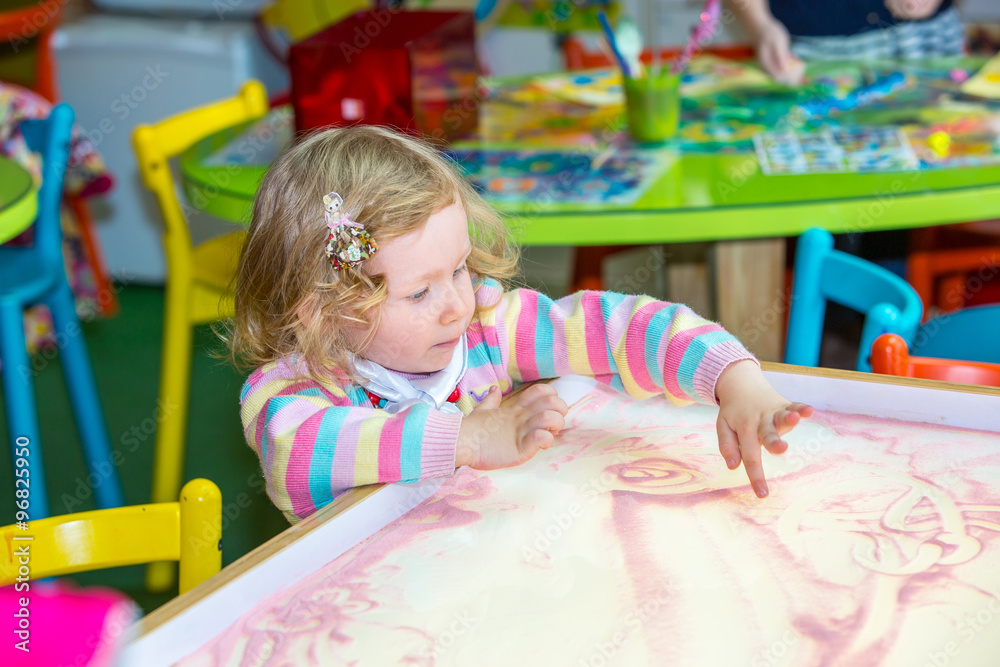 Cute child girl drawing draws developing sand in preschool at table in kindergarten by method of Montessori Cute child girl drawing draws developing sand in preschool at table in kindergarten by method of Montessori