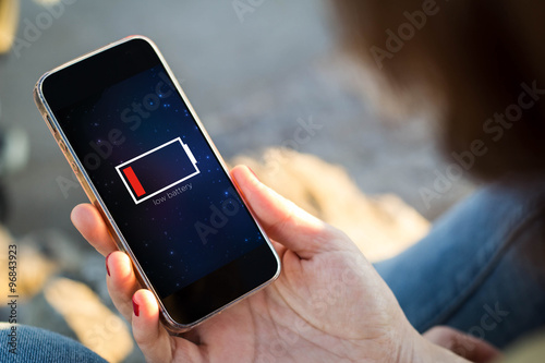 Foto woman sitting in the street holding her smartphone with low batt