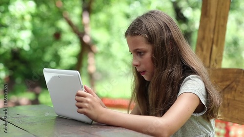 Beautiful girl with tablet computer sits on the bench in summerhouse. Angry girl with Tablet-PC sits on the bench in bower. True sincere emotions. Girl playing the game on his tablet computer
