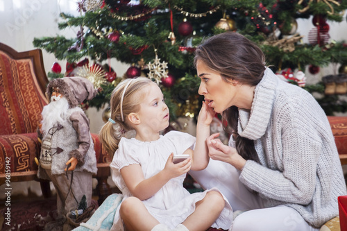 Mother and daughter in front of Christmas tree, opening presents © nikodash