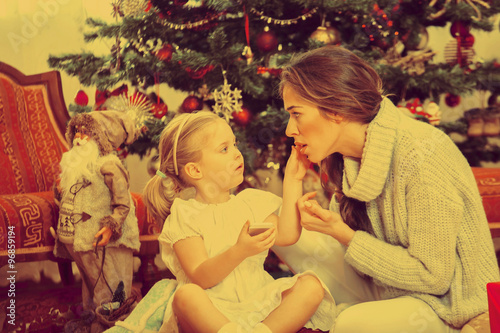 Mother and daughter in front of Christmas tree, opening presents © nikodash