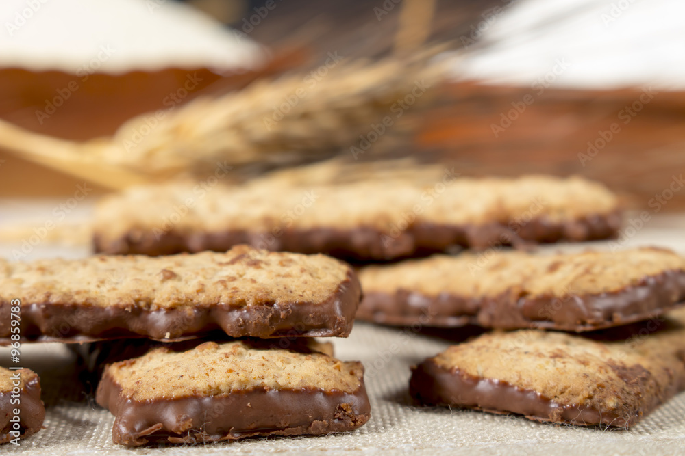 Biscuits with chocolate in front of wheat spikes and pastry flour. Confectionery.