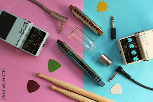 Music concept - guitar pedals, drum sticks, harmonica, audio plug, guitar slide and guitar picks on half blue half pink background