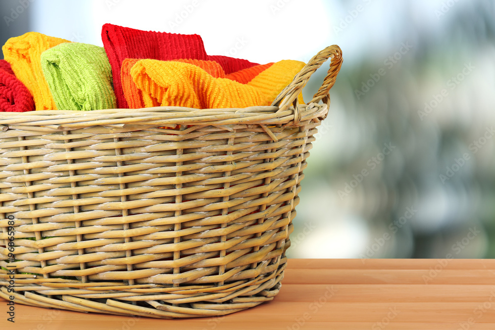 Colorful towels in basket on bright background