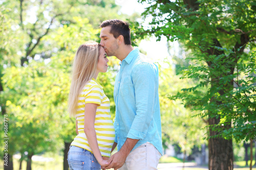 Canvastavla Expectant couple holding hands, man kissing pregnant woman's forehead in a park,