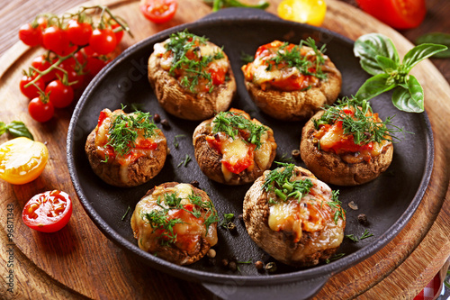 A frying pan with stuffed mushrooms and vegetables on the table