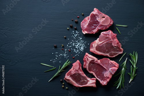 Fotografie, Obraz Surové jehněčí steaky T-bone s kořením na černém povrchu dřeva