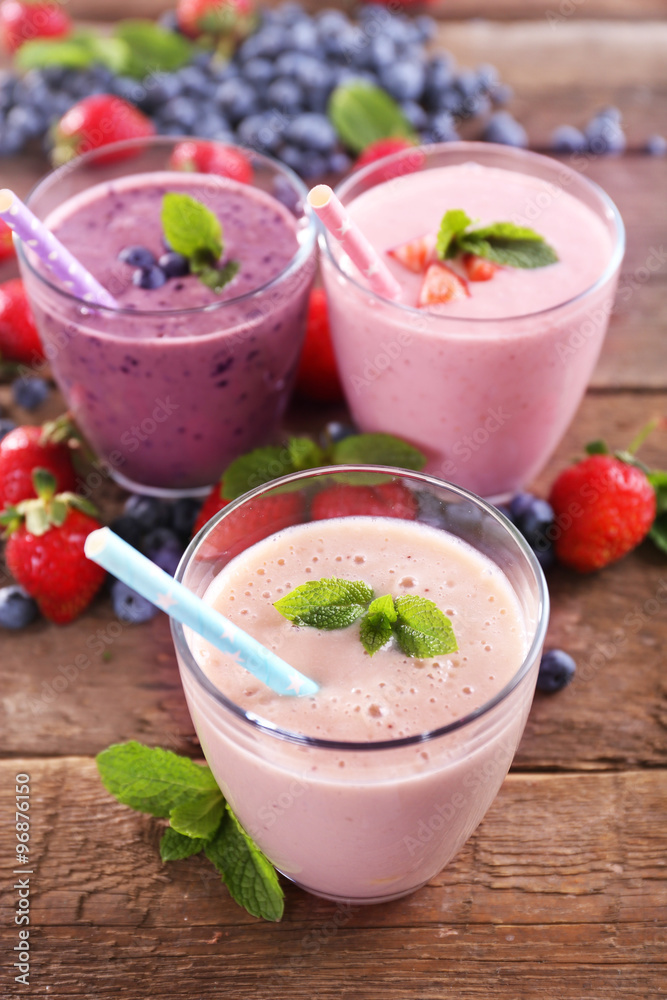 Tasty blueberry, strawberry and milk yogurts in a row decorated with berries and mint on wooden background, close up Tasty blueberry, strawberry and milk yogurts in a row decorated with berries and mint on wooden background, close up