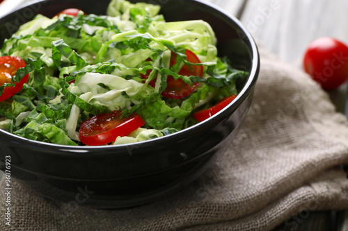 Savoy cabbage and tomato salad served in bowl on wooden table