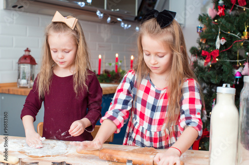 Adorable girls baking gingerbread cookies for Christmas at home kitchen