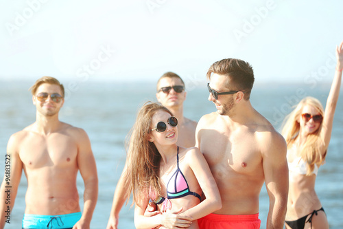 Happy couple and their playful friends relaxing at the beach, outdoors