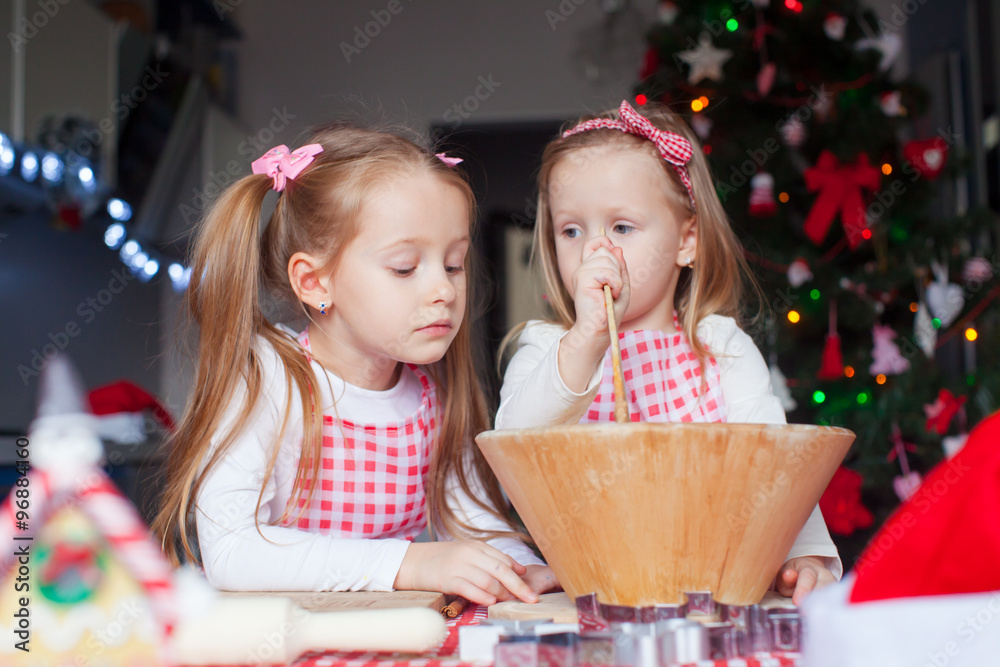 Adorable girls baking gingerbread cookies for Christmas at home kitchen