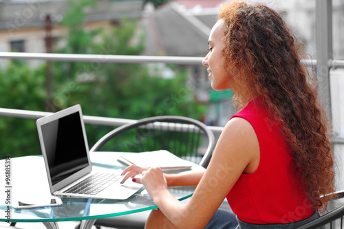 Young pretty business woman in red dress with laptop at summer terrace