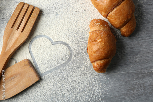 Heart of flour, croissant and wooden kitchen utensils on gray background