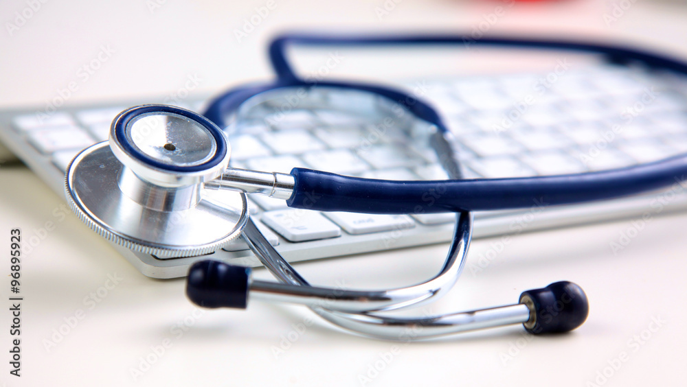 A medical stethoscope near a laptop on table, on white A medical stethoscope near a laptop on table, on white