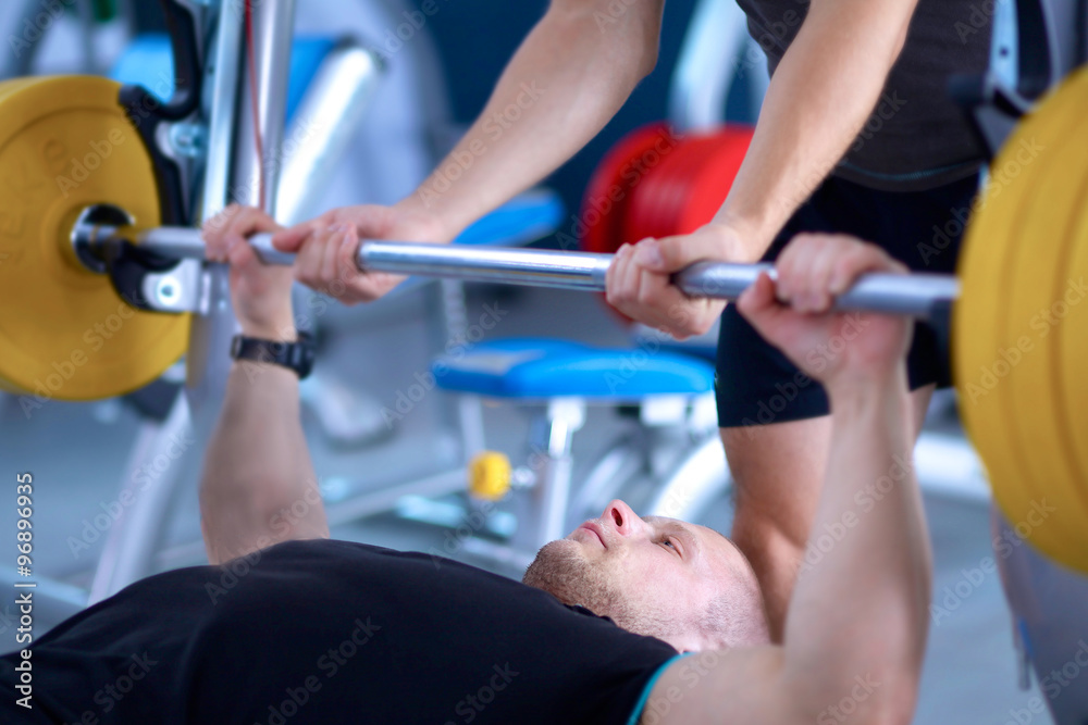 Fototapeta premium Young man lifting the barbell in gym with instructor