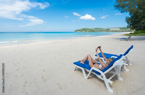 Tropical vacation. Young beautiful woman relaxing alone on the beach and make selfie with smartphone. 