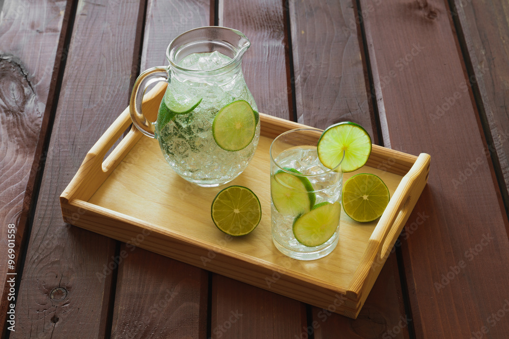 Drink and jug on wooden tray with ice and condensation on glass