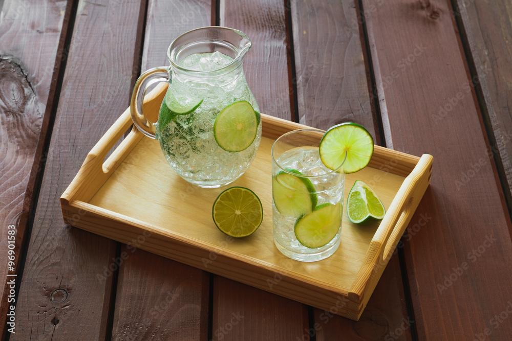 Drink and jug on wooden tray with ice and condensation on glass