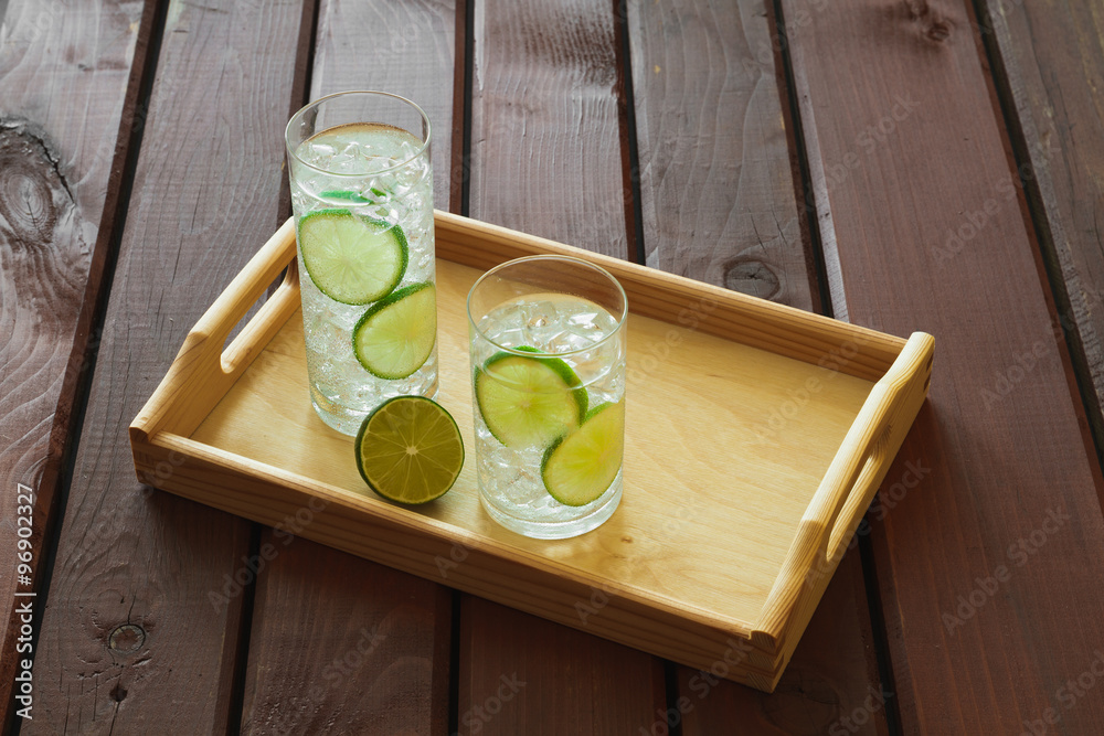 Two drinks on wooden tray with ice and condensation on glass