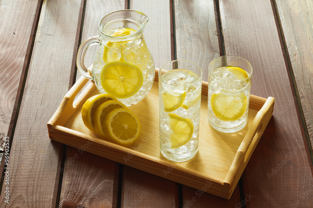 Two drinks and jug on wooden tray with ice and condensation on g