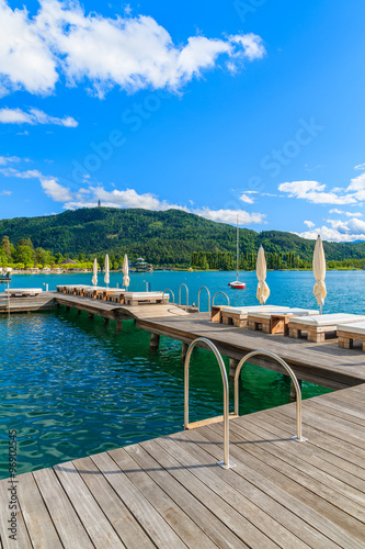 Sunchairs on wooden pier and view of beautiful alpine lake Worthersee in summer, Austria
