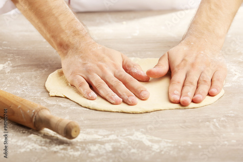 Hands preparing dough basis for pizza on the wooden table, close-up © Africa Studio